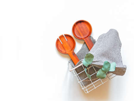 A wide wooden fork and a spoon for serving salad, a waffle gray towel and a branch of eucalyptus are...