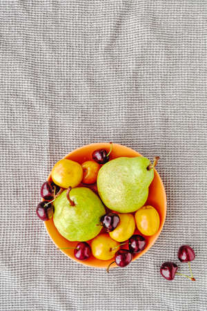 Fruit and berry composition. Green pears, ripe cherries and apricots are in an orange plate on a...