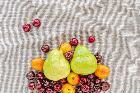 Fruit and berry composition. Green pears, ripe cherries and apricots are on a gray waffle towel....