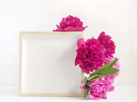 Flower composition. Layout with empty wooden photo frame and lush red and pink peonies. Drops of water are on the petals. Light background. Copy space.の写真素材