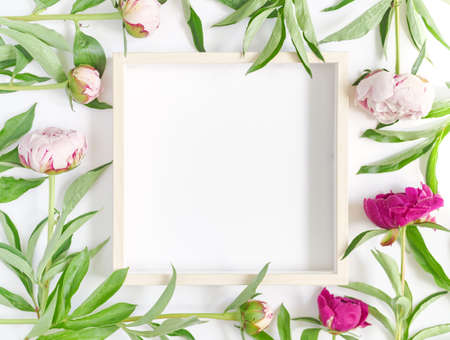 An empty wooden picture frame and fresh peonies are on a white background. Flower composition. Flat...