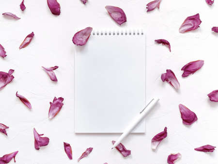 Petal composition. An open blank notebook and a white pen are on a white textured background. The layout is decorated with flower petals. Top view. Flat lay. Copy space.の写真素材