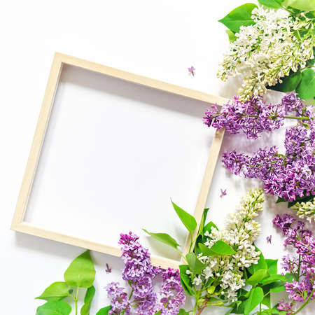 Flower composition. Empty wooden picture frame and branches of blooming lilacs are on a white...