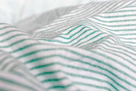 Close view of crumpled bedding. Green striped cotton fabric. Cloth washing and laundry concept at home. Change of bed linen to clean.の写真素材