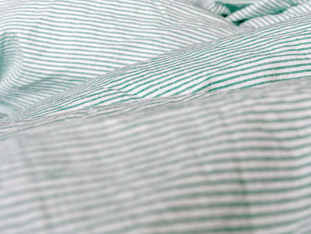Close view of crumpled bedding. Green striped cotton fabric. Cloth washing and laundry concept at home. Change of bed linen to clean.の写真素材