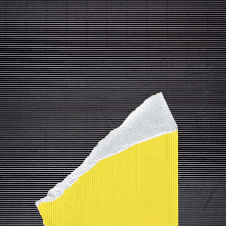 A piece of torn yellow corrugated cardboard is on black textured paper. Abstract image for banner. Flat lay. Copy space.の写真素材