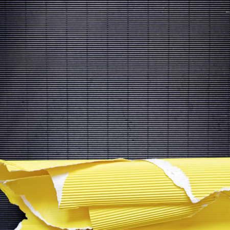 A piece of torn yellow corrugated cardboard is on black textured paper. Abstract image for banner. Flat lay. Copy space.の写真素材