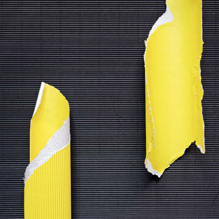 A piece of torn yellow corrugated cardboard is on black textured paper. Abstract image for banner. Flat lay. Copy space.の写真素材