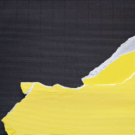 A piece of torn yellow corrugated cardboard is on black textured paper. Abstract image for banner. Flat lay. Copy space.の写真素材