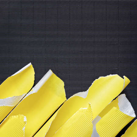 A piece of torn yellow corrugated cardboard is on black textured paper. Abstract image for banner. Flat lay. Copy space.の写真素材