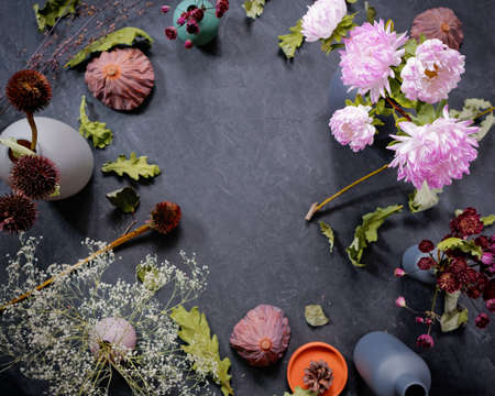 Autumn flower arrangement. A bouquet of asters is in a vase. There are various dried flowers and oak leaves nearby. Dark concrete background. Autumn concept. Birthday card. Flat lay. Top view.の写真素材