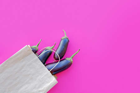 Whole, ripe eggplants are in a paper bag on a purple background. Autumn vegetable concept, harvesting. Flat lay. Top view. Copy space.の写真素材