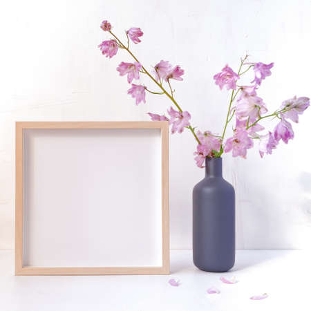 Autumn flower arrangement. Fresh delphinium flowers are in a bottle vase. There is an empty wooden photo frame nearby. Copy space.の写真素材