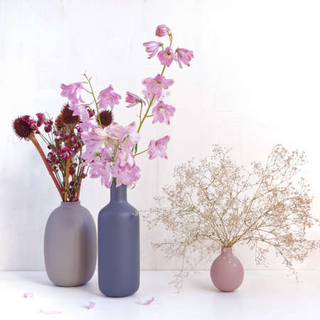 Autumn flower arrangement. Fresh delphinium flowers are in a bottle vase. There are dried flowers nearby in other vasesの写真素材