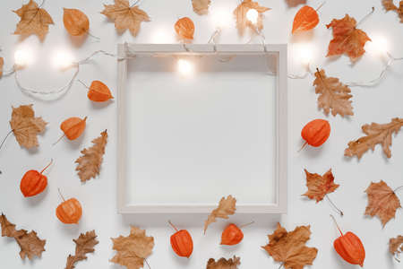 Mockup of dried oak leaves, maple leaves, physalis flowers, glowing garland and wooden photo frame. Autumn, fall, thanksgiving day concept. Gray background. Flat lay, top view, copy space.の写真素材