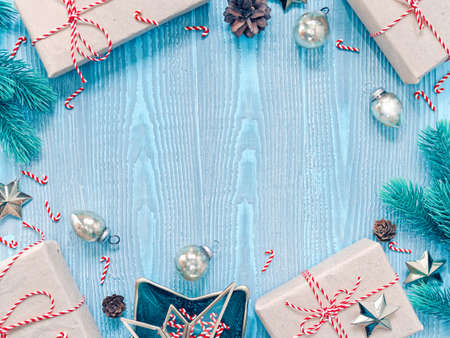 Christmas composition. Gifts in craft paper are tied with a striped ribbon. Coniferous branches, cones and decorations are nearby. Blue wooden background. Flat lay, top view, copy space.の写真素材