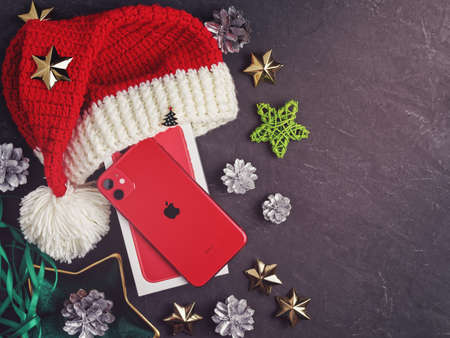 Moscow, Russia - December 17, 2019: A red iPhone 11 is on a dark background. Nearby are Christmas decorations. New Year holidays gift concept. Flat lay. Copy space.のeditorial素材