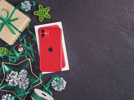Moscow, Russia - December 17, 2019: A red iPhone 11 is on a dark background. Nearby are Christmas decorations. New Year holidays gift concept. Flat lay. Copy space.のeditorial素材