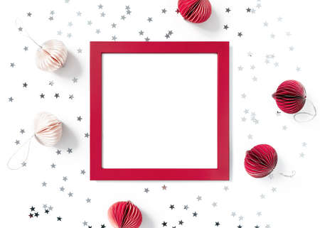 Christmas composition. Empty red wooden frame, paper Christmas decorations, star-shaped confetti are on a white background. New Year, winter concept. Greeting card. Flat lay, top view, copy space.の写真素材