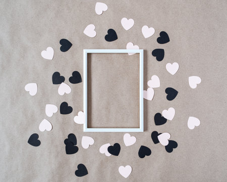 Blank white photo frame and heart-shaped confetti are on rough brown paper. Minimalistic layout for...