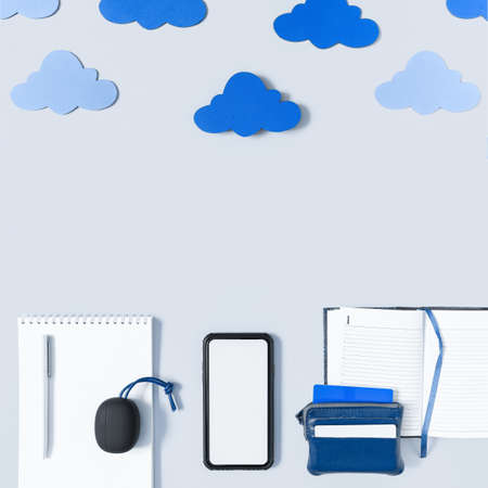 Cloud sync concept, office in the cloud. A blank screen smartphone, wireless headphones, a notebook with a pen, a to-do list and a wallet with credit cards are under the clouds. Flat lay. Copy space.の写真素材