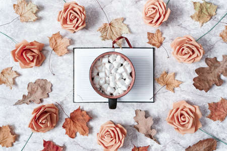 Autumn composition. A large mug with marshmallows, an open notebook, dried maple leaves and roses...