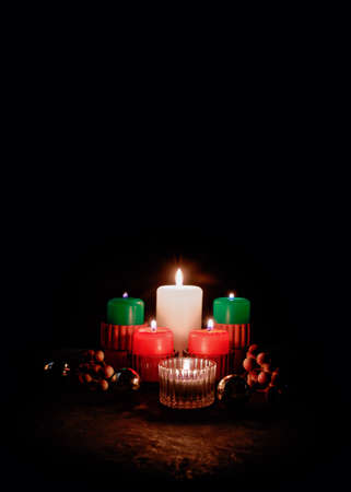 Christmas composition in a minimalist style. Burning wax candles of red, green and white colors are in candlesticks. There are shiny balls and bunches of berries nearby. Copy space.の写真素材