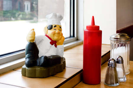 Figure of a cook lying in a lazy pose, smiling, on a table with saltcellar, pepper box, sugar pot, ketchup の写真素材