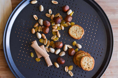 Peanuts, hazelnuts, pistachios, yellow raisin, jam sticks, baguettes, on a black baking pan with holesの写真素材