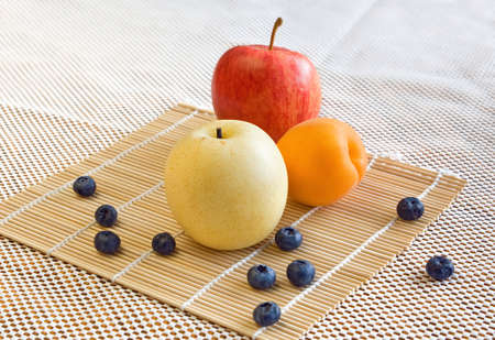 Ripe delicious red apple, asian yellow pear and apricot with blueberries around on a bamboo mat on a white background.の写真素材
