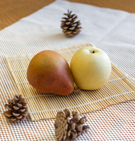 Asian yellow pear and belgian brown pear with pine cones on bamboo mat and white background. Selective focus.の写真素材
