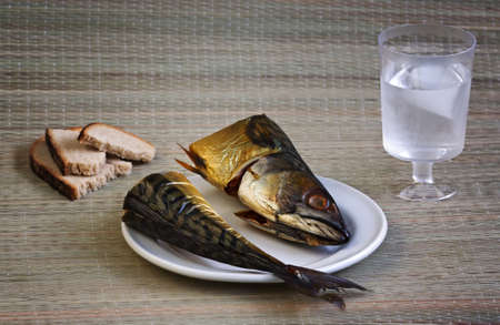 Closeup shot of mackerel head and tail on a white plate with bread and a glass of cold water. Selective focus.の写真素材