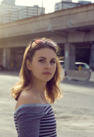 Portrait of a girl in striped shirt with sunglasses on her head looking straight into the camera at sunsetの写真素材