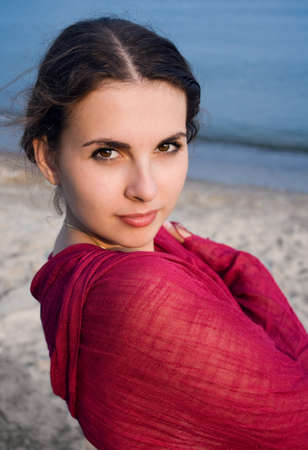 Closeup portrait of a young boho girl with a pink shawl on a beach near the waterの写真素材