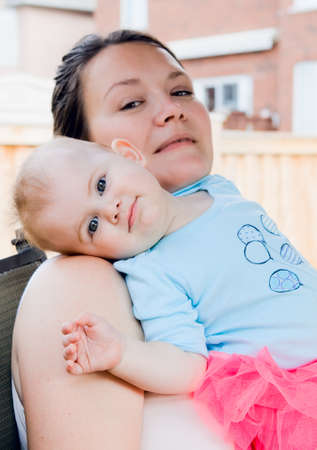 Portrait of mother with daughter relaxing on her shoulder smiling outdoor backyard summerの写真素材