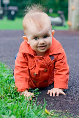 Portrait of a cute baby in red trench crawling on a playground outdoorの写真素材