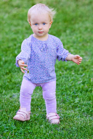 Small sweet baby girl, standing with flower on a meadow, summer day.の写真素材