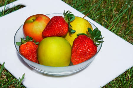 Plate with yellow, red apples and strawberries on grass, summerの写真素材