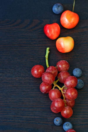 Grapes, cherry, blueberry on black wooden background with copy space, summer, autumn harvestの写真素材