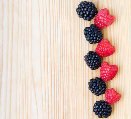 Closeup of ripe blackberries and red pink raspberries with on light wooden board background, funny...