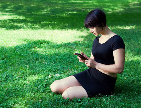 Portrait of a young lady girl woman with black short pixie haircut sitting on grass on field meadow...