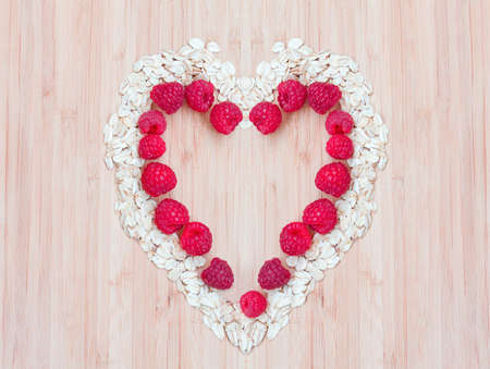 Heap of raw oatmeal flakes with raspberries in a shape of heart on a wooden cutting board, fresh...