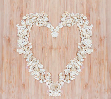Heap of raw oatmeal flakes in a shape of heart on a wooden cutting board, fresh morning breakfast, dietの写真素材
