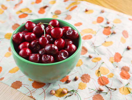 Closeup still life of a bowl full of red sweet cherries on a wooden table, rustic tablecloth, with stems and pits on the backgroundの写真素材