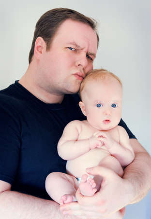 Young father holding white caucasian baby with blue eyes in his arms making funny face expression in studio, lifestyle, family portraitの写真素材