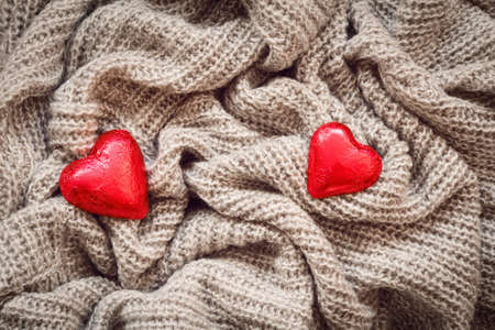 Closeup macro texture of knitted wool fabric material with red candy hearts on top, clothing background with wrinkles and folds, Valentine holiday card, love conceptの写真素材