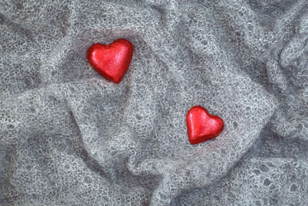 Closeup macro texture of grey knitted wool fabric material shawl scarf with red candy hearts on top, clothing background with wrinkles and folds, Valentine holiday card, love conceptの写真素材