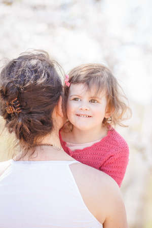 Close up portrait of caucasian mother in white dress holding hugging her daughter in pink clothes on sunny spring summer day in the park outsideの写真素材