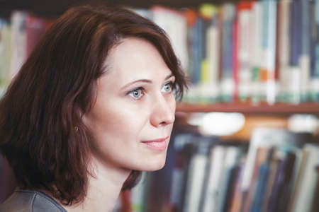 Closeup portrait of thoughtful middle age mature woman student in library looking away from camera,...