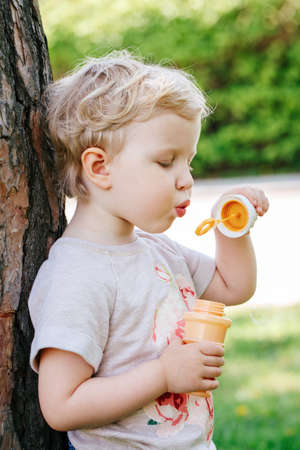 Portrait of cute funny little blond Caucasian child girl toddler standing in the green forest field...